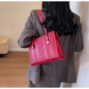 Detail of red embossed leather tote bag with gold lettering shown on model's shoulder