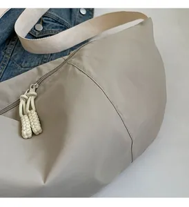 Close-up of beige nylon crescent bag featuring a woven zipper pull and wide fabric strap