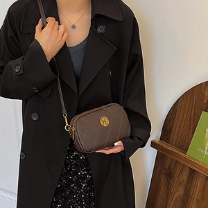 Sac à bandoulière matelassé marron foncé avec emblème doré porté par un modèle