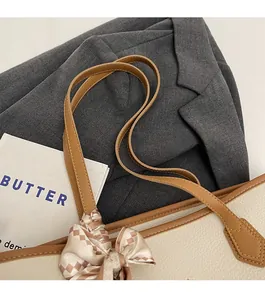 Detail of off-white tote bag showing brown leather handles and silk scarf decoration