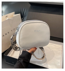 Detail of white pebbled leather round bag with geometric strap in a black gift box
