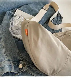 Detail of beige nylon crossbody bag with orange woven label and white strap on denim jacket