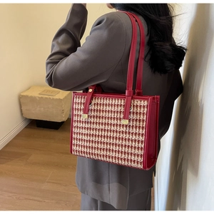Macro detail of red houndstooth tote bag showing leather handles and gold metal hardware