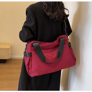 Sac de voyage en nylon bordeaux porté à l'épaule par un mannequin en manteau