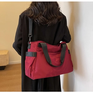 Détail du sac de voyage en nylon rouge avec poignées noires et bandoulière réglable