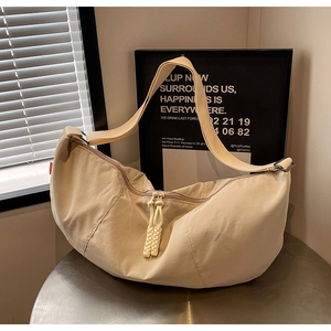 Close-up of beige nylon crescent bag featuring a woven rope zipper and wide strap