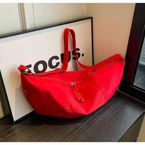 Detail of red nylon half-moon crossbody bag with woven zipper pull on a dark wood surface