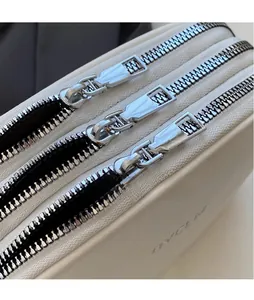 Detail showing three parallel silver metal zippers on white crossbody bag