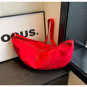 Detail of red nylon crescent bag with wide woven strap and knot zipper pull on wood