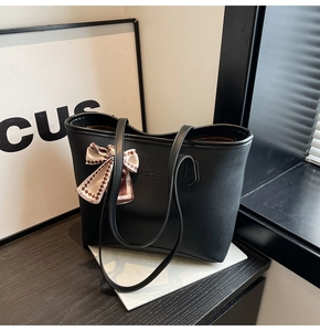 Detail of black pebbled leather tote bag featuring a decorative fashion bow scarf