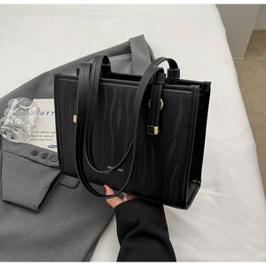 Close-up of black wave-embossed tote bag with gold metal logo and minimalist styling