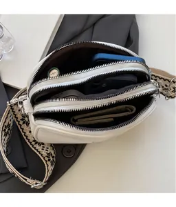 Detailed view of white crossbody bag featuring three zippered layers and wide strap