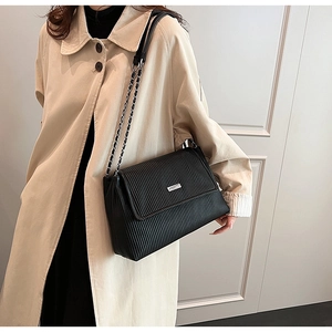 Close-up of black pleated tote bag with silver metal buckle and chain strap on beige trench coat