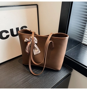 Detailed close-up of brown litchi grain leather tote bag with stylish plaid scarf detail