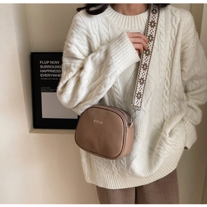 Chic brown pebbled leather crossbody bag with geometric woven strap on a white sweater