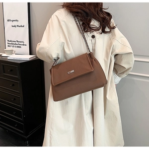 Detail of a brown pleated tote bag with chain strap worn by a model in a modern room