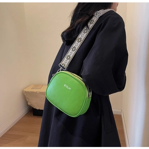 Detail view of bright green textured leather camera bag with wide patterned shoulder strap