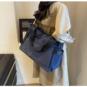 Vue latérale d'un grand sac de voyage en tissu Oxford bleu marine avec bandoulière sur modèle