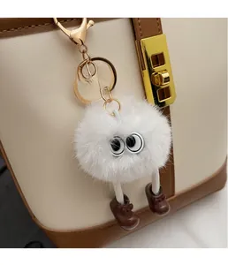 Close-up of white plush doll charm with cartoon eyes on a leather bucket handbag