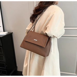 Close-up of pleated brown crossbody tote bag with chain strap on a beige trench coat