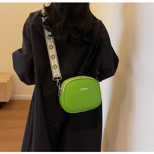Green crossbody round bag with patterned wide strap worn over a black coat detail