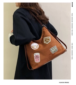 Detail of brown suede tote bag featuring colorful embroidered patches and leather strap