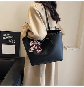 Detail of black pebbled leather tote bag with a fashion silk scarf bow on the handle