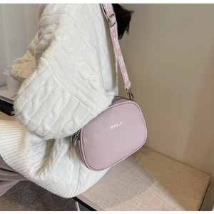 Detail of pink crossbody camera bag with wide patterned strap on white sweater