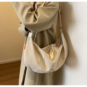 Detail of beige nylon crescent bag featuring a woven rope zipper and orange side label