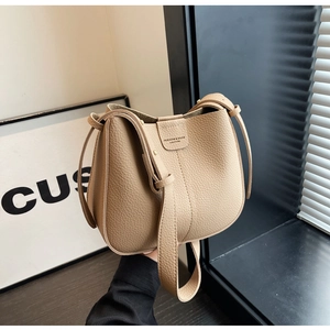 Détail de la texture cuir grainé et des boucles dorées du sac seau de couleur beige clair