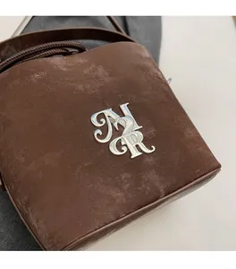Détail du sac seau en daim marron foncé avec monogramme métallique argenté chic
