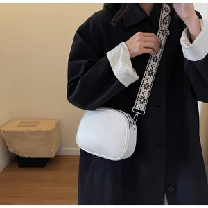 Detail of white lychee leather camera bag featuring embroidery wide strap and BYELM logo