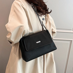 Elegant black pleated shoulder bag with chain strap shown on model in a beige coat