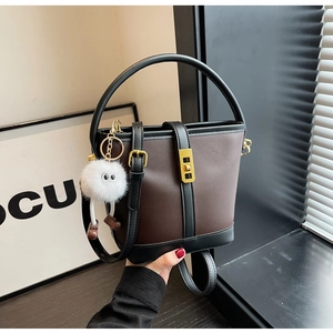 Detailed close-up of dark brown bucket bag with metal buckle and plush monster charm