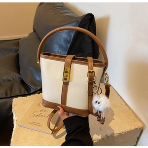 Detail view of two-tone bucket bag with gold twist lock and plush eye charm on leather sofa