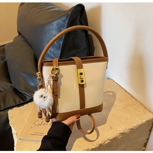 Detail of a vintage cream and brown leather bucket bag with gold lock and plush charm