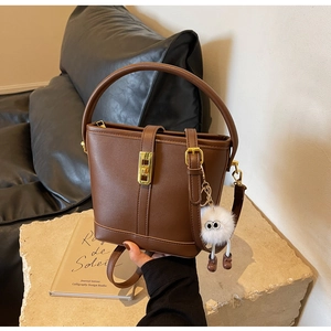 Detail view of dark brown bucket bag with gold turn-lock and plush charm on stone base