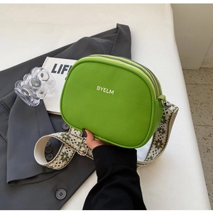 Detail of bright green faux leather crossbody bag with white logo and jacquard strap
