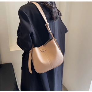 Détail du sac seau en cuir beige avec coutures décoratives sur un manteau noir