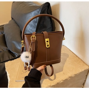 Detail of dark brown leather bucket bag with gold hardware and plush charm on stone pedestal