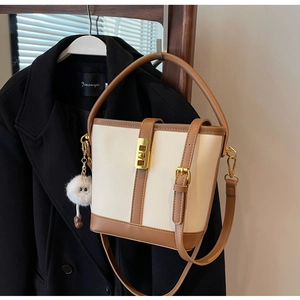 Detail view of a cream and brown bucket bag with a plush charm hanging on a coat rack