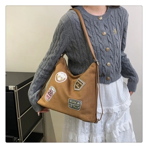 Detail of a brown suede tote bag with vintage patches worn by a model in casual attire