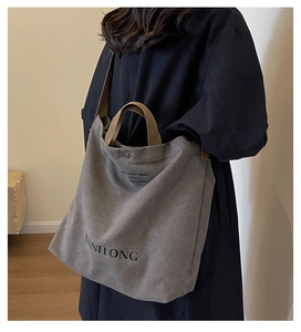 Detail of grey canvas tote bag with brown straps shown on shoulder for size reference