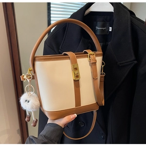 Detail of a two-tone bucket bag with metal twist lock and cute plush monster charm