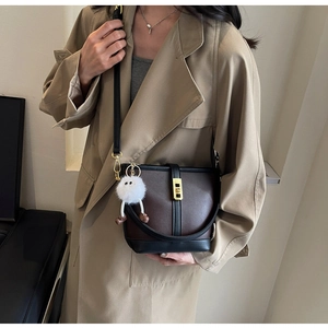 Close-up of brown bucket bag with gold clasp and cute plush doll keychain charm