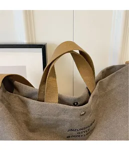 Close-up of khaki canvas tote bag featuring secure metal snap closure and woven handles