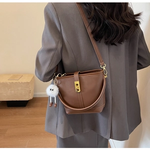 Detail view of brown bucket bag with gold hardware and white plush charm on model