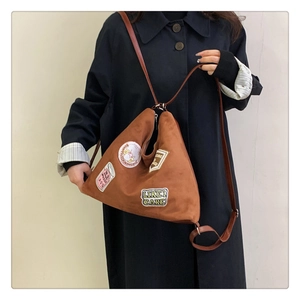 Detail of a brown triangular tote bag featuring retro embroidered patches and high-quality suede