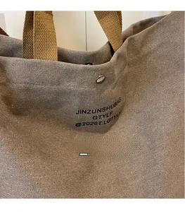 Close-up of grey canvas tote bag with woven handles and silver snap button closure