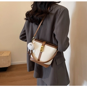 Detail of color-block bucket bag with gold lock and plush charm on grey blazer